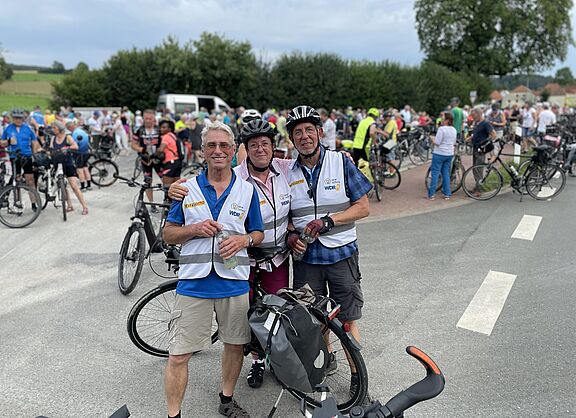 Die drei ADFC-Scouts mit Flaschen in der Hand stehen vor einer Menge an Radfahrerinnen und Radfahrern.