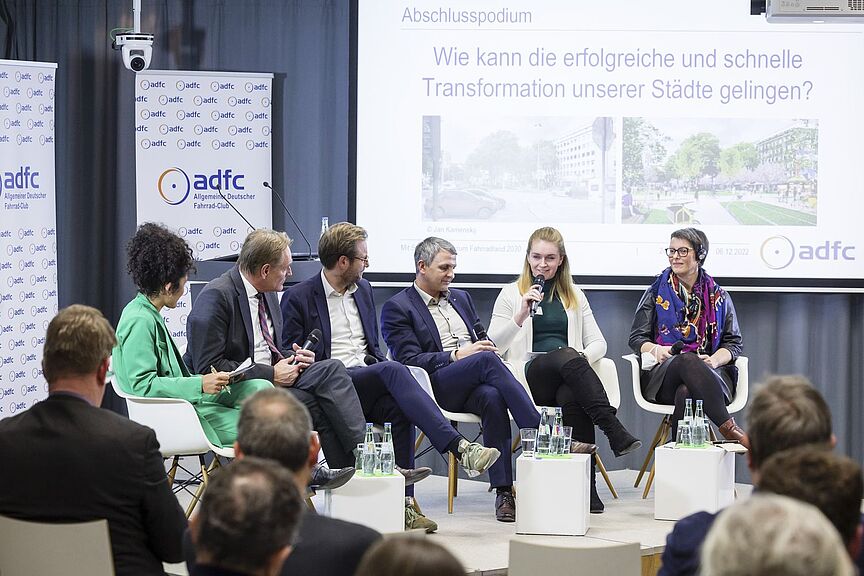 ADFC-Symposium „Mit Schnellausbau zum Fahrradland 2030“ am 6. Dezember 2022 Bild von einem Podium mit den Teilnehmenden einer Podiumsdiskussion.